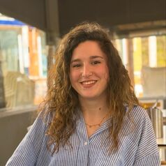 Young woman with wavy hair smiling at the camera, wearing a blue striped shirt.