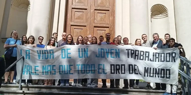 Group of people on steps holding a banner that reads 'La vida de un joven trabajador vale más que todo el mundo'.