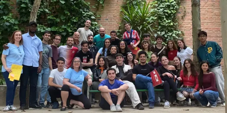 Large diverse group of students posing together outdoors against a brick wall with greenery in the background.