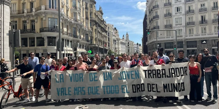Group of protesters standing in a city street, holding a banner that reads 'La vida de un joven trabajador vale más que todo el oro del mundo.'
