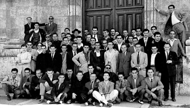 Large group of men in suits posing on the steps of a stone building.