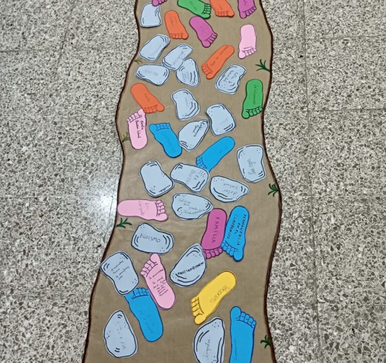 Colorful paper footprints and stone shapes laid on a wavy beige mat on a speckled floor, forming a winding path.