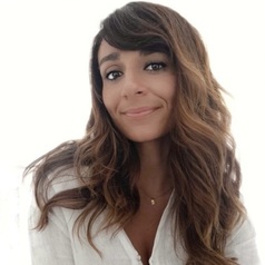 Smiling woman with wavy brown hair wearing a white top, looking at the camera.