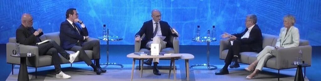 Panel de cinco personas sentadas en un escenario con fondo azul; título en español sobre construcción y servicio, entre ellos tres hombres y dos mujeres discuten en sillones y una mesa central.
