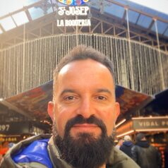 Man with a beard taking a selfie outside a souvenir shop storefront with a sign overhead.