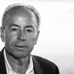 Black-and-white portrait of a middle-aged man with short hair, wearing a blazer and collared shirt, looking slightly to the left.