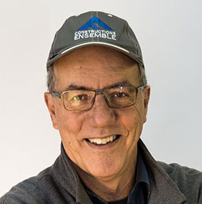 Smiling man wearing glasses and a gray cap that reads 'Construction Ensemble'.
