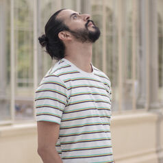 Young man with a striped t-shirt gazing upward outdoors beside a glass-fronted building.