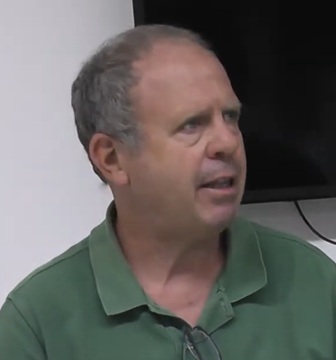 Man with short gray hair in a green polo shirt speaking in an indoor setting.